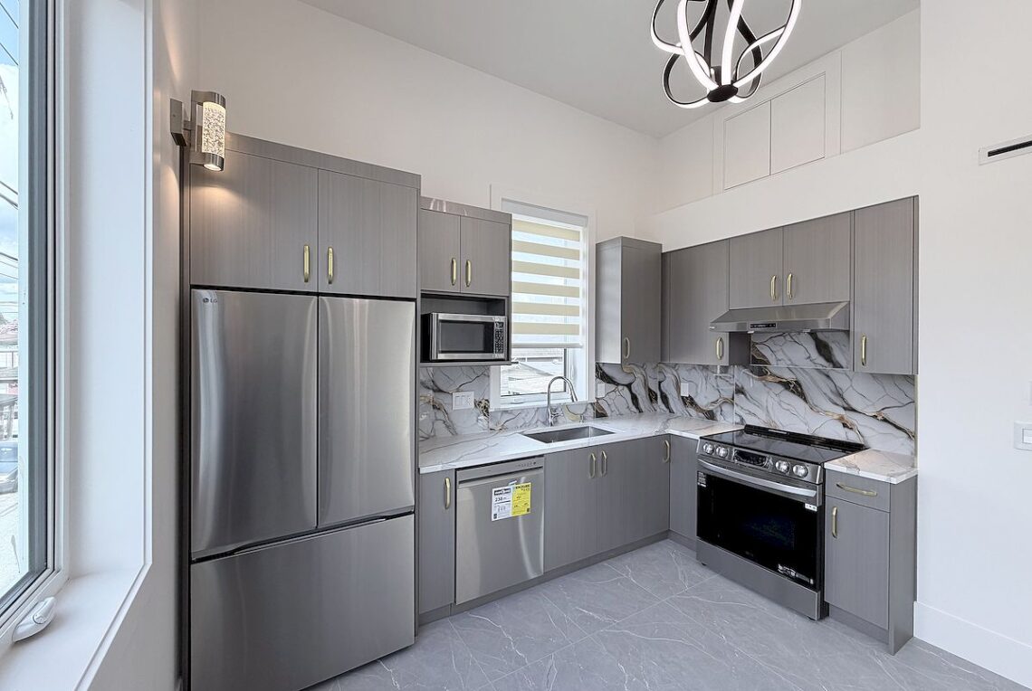2 Bed 2 Bath Coach House in Vancouver East (Near Moberly Park) 溫東2房後巷屋近 Moberly 公園 | Selling & Managing Vancouver Real Estate Modern L-shaped kitchen with gray cabinets, stainless steel fridge, dishwasher, microwave, and oven with marble backsplash and countertops.