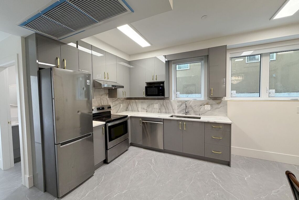 Ground Floor 2-Bed Suite in Vancouver East (Near Moberly Park) 溫東平地兩房套房近 Moberly 公園 | Selling & Managing Vancouver Real Estate Modern gray kitchen with stainless steel fridge, oven, microwave, and marble countertops.