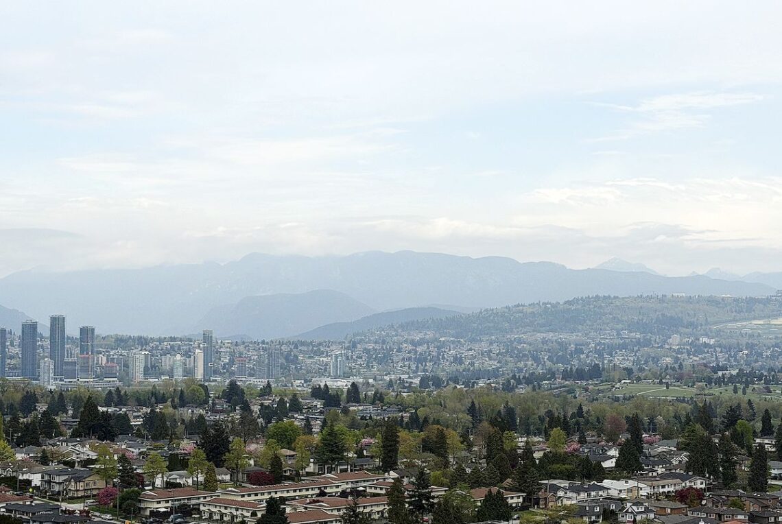 Vancouver East 1 Bed 1 Den Condo w/ AC & Mountain View 溫東一睡房加書房高層山景公寓 | Selling & Managing Vancouver Real Estate Cityscape with a residential foreground and skyline; distant blue mountains under a pale sky