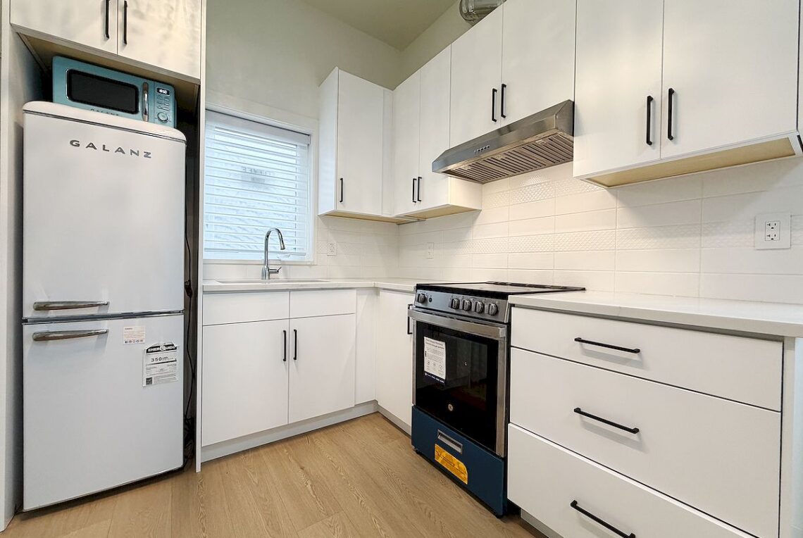 Brand New 1-BR Private Suite with Separate Entrance in Richmond Quilchena 列治文 Quilchena社區全新落成獨立屋一臥室一衛套房火熱招租 | Selling & Managing Vancouver Real Estate White modern kitchen with a Galanz fridge in the left alcove, turquoise microwave on top, and white cabinets throughout.
